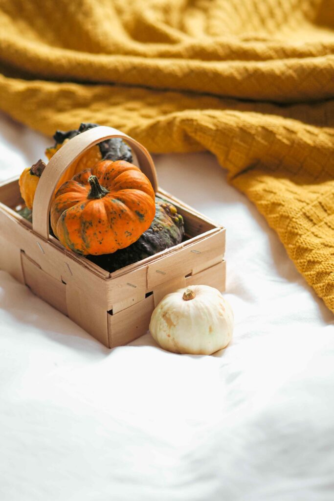 Woven basket filled with pumpkins and cozy blankets beside a beautifully styled autumn bed